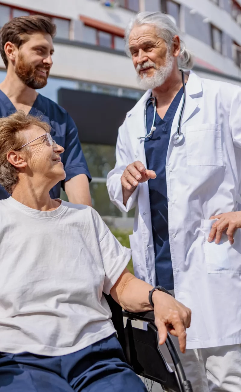 A doctor and nurse talking with a patient using a wheelchair
