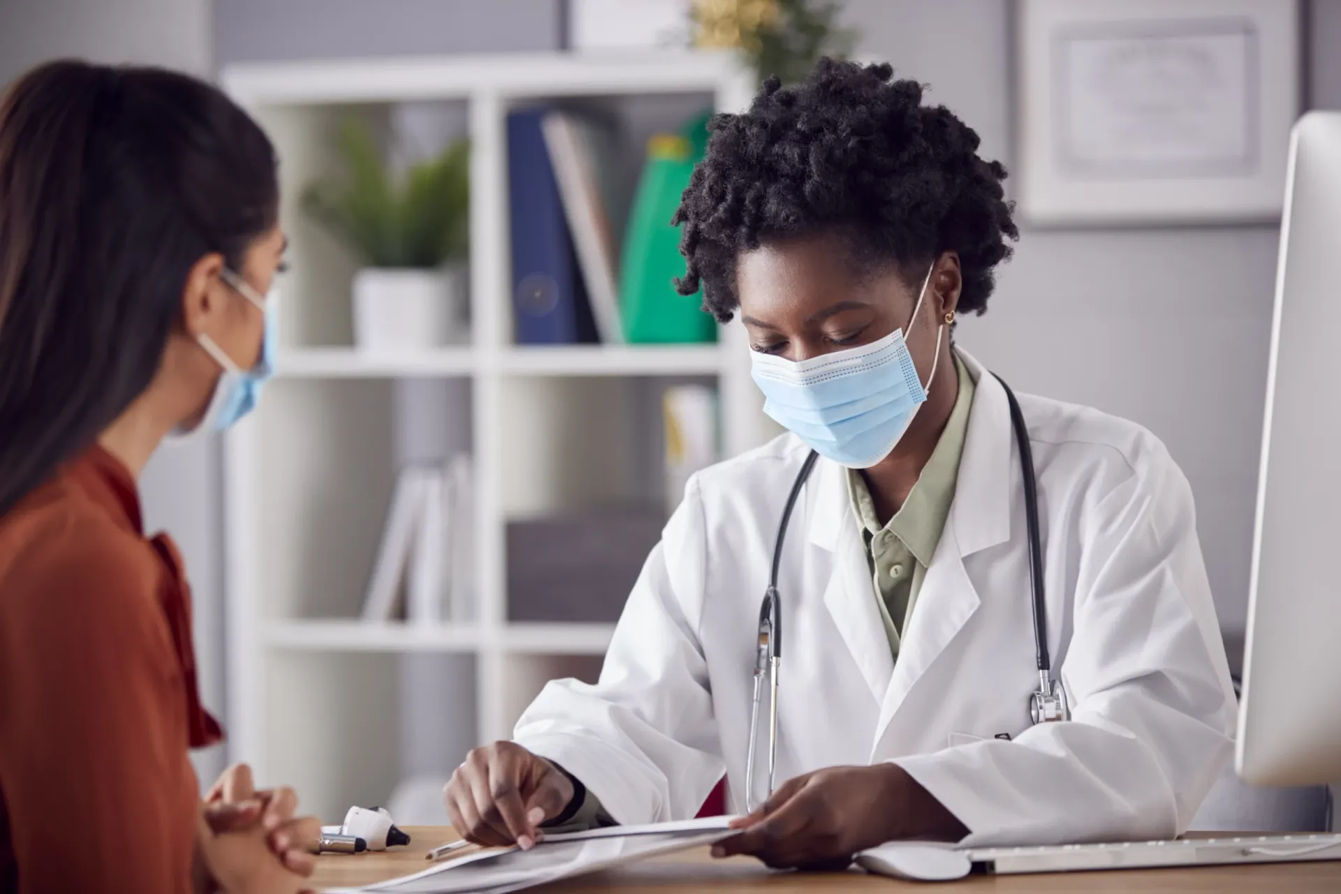 A doctor in a white coat and face mask during a consultation
