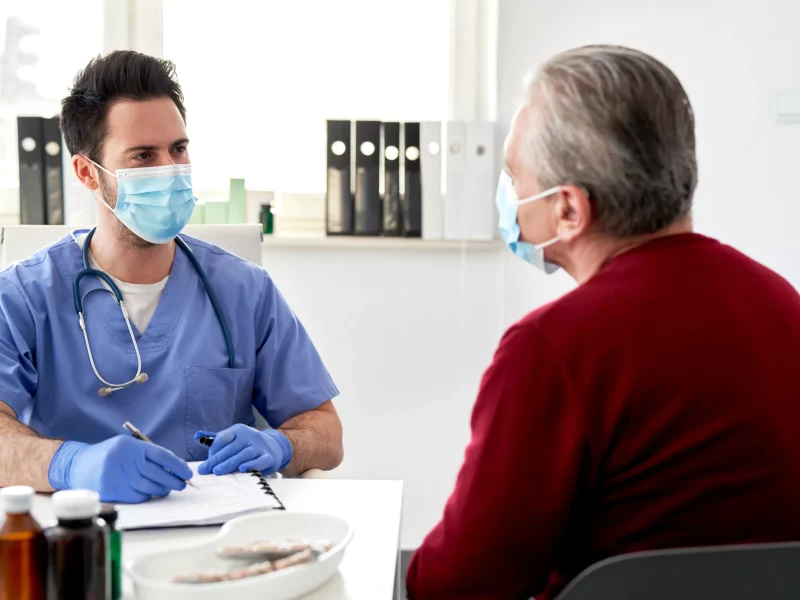 A doctor in a protective mask talking with a senior patient