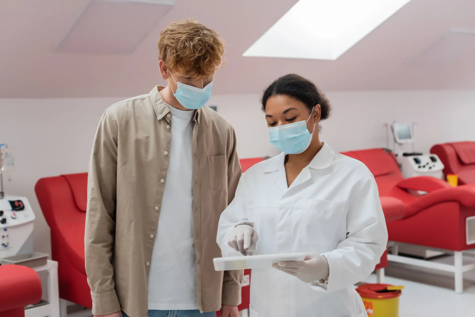 A doctor in a medical mask pointing at a digital tablet with a patient